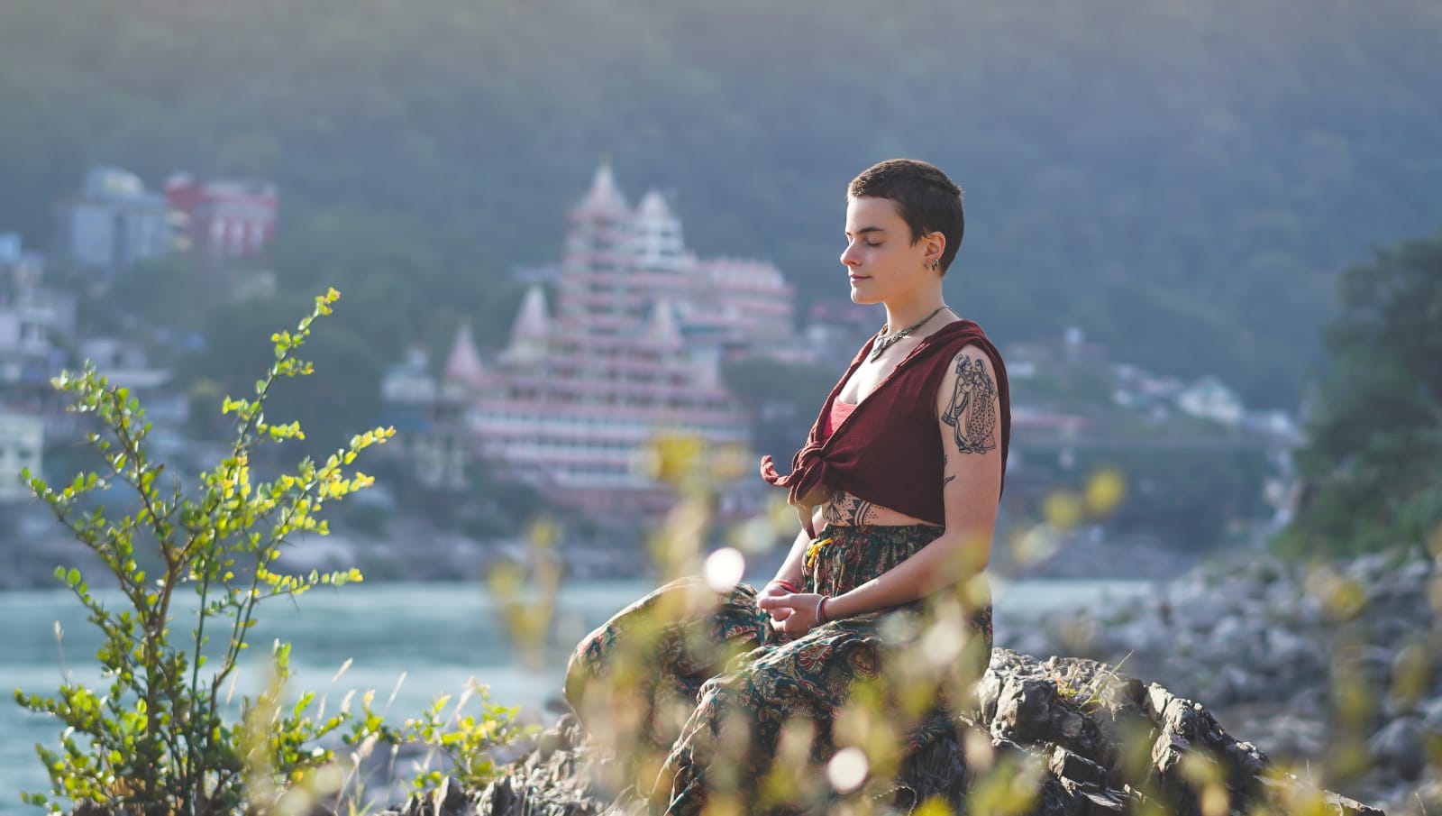 Person practising guided meditation beside a riverside in a peaceful setting.